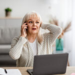 old woman worried on cellphone in front of laptop