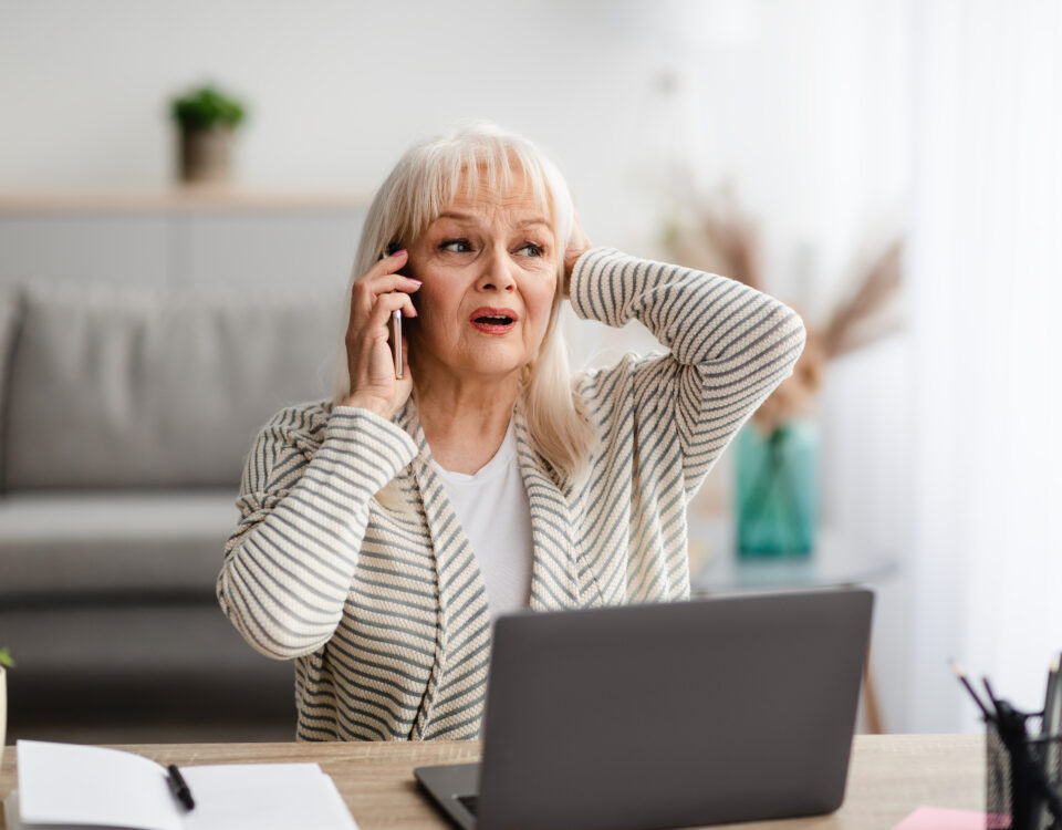 old woman worried on cellphone in front of laptop