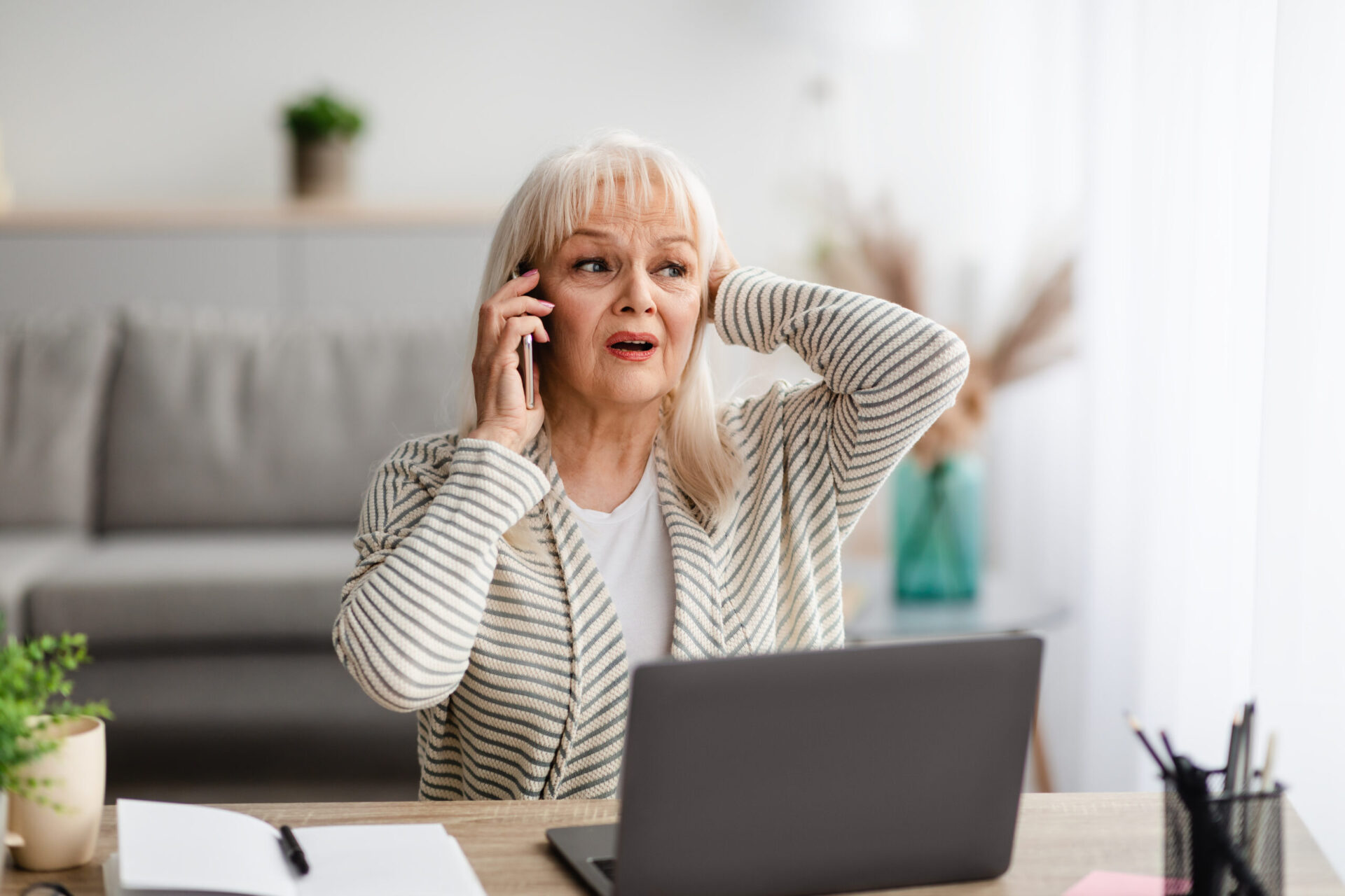 old woman worried on cellphone in front of laptop